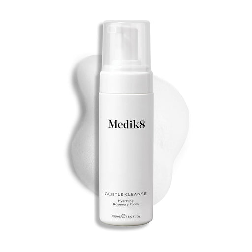 A Medik8 Gentle Cleanse pump bottle displayed on a white background with a smear of white foam behind it, highlighting the product's hydrating texture.