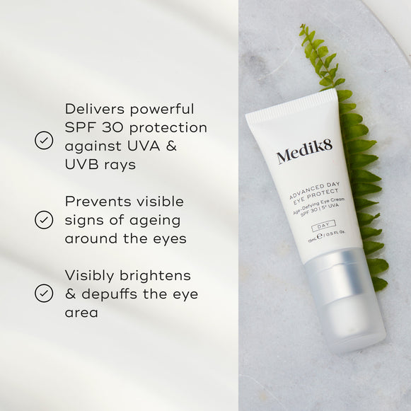 Advanced Day Eye Protect tube lies on a marble surface next to a green fern leaf. Text highlights its SPF 30 protection, prevention of visible ageing signs, and its ability to brighten and depuff the eye area.-hover-5