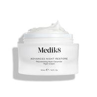 Medik8 Advanced Night Restore cream jar shown open with a rich dollop of white cream peaked on top against a clean white background, highlighting its smooth, restorative texture. Black text on the jar reads 
