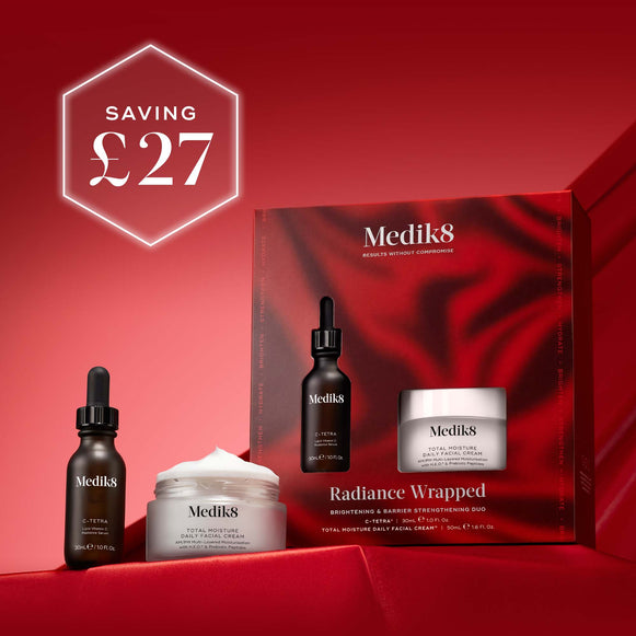 A large, hero image displaying two Medik8 skincare products – a dark dropper bottle and a white jar – on a deep red, rippled fabric background. The text 'Medik8' is visible at the top and on the product labels. Below the products, 'RADIANCE WRAPPED' is displayed, with 'BRIGHTENING & DAILY MOISTURE' and 'TOTAL MOISTURE DAILY FACIAL CREAM' below it.-79
