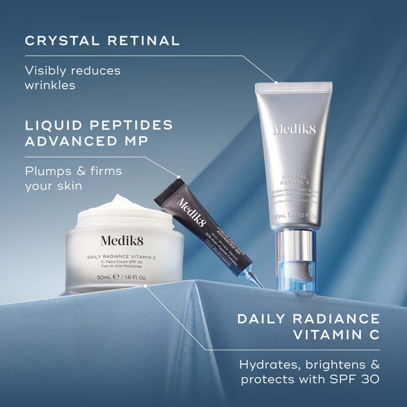Three Medik8 skincare products, a white jar, a black tube, and a silver pump bottle, arranged on a light blue, rippled fabric background. The text 'AGE-DEFYING & RADIANCE BOOSTING TRIO' is at the top, with smaller text below: 'Peptides + Moisturiser' and 'Vitamin A'
-hover-78