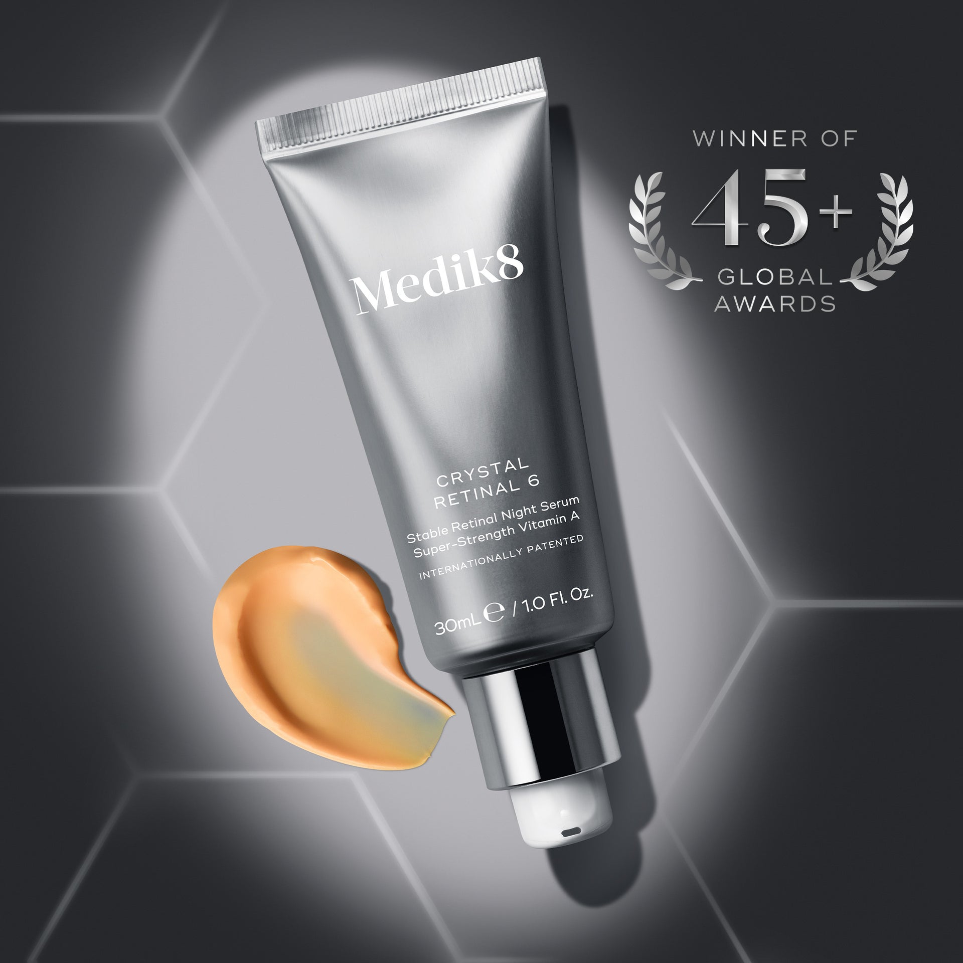 A professional photograph of a grey Crystal Retinal 6 tube against a grey hexagonal patterned background. To the bottom left of the tube is an orange serum swirl texture. To the top right of the tube are laurels with text that reads, ‘WINNER OF 45+ GLOBAL AWARDS’. A white call-to-action button at the bottom reads, ‘SHOP CRYSTAL RETINAL’.