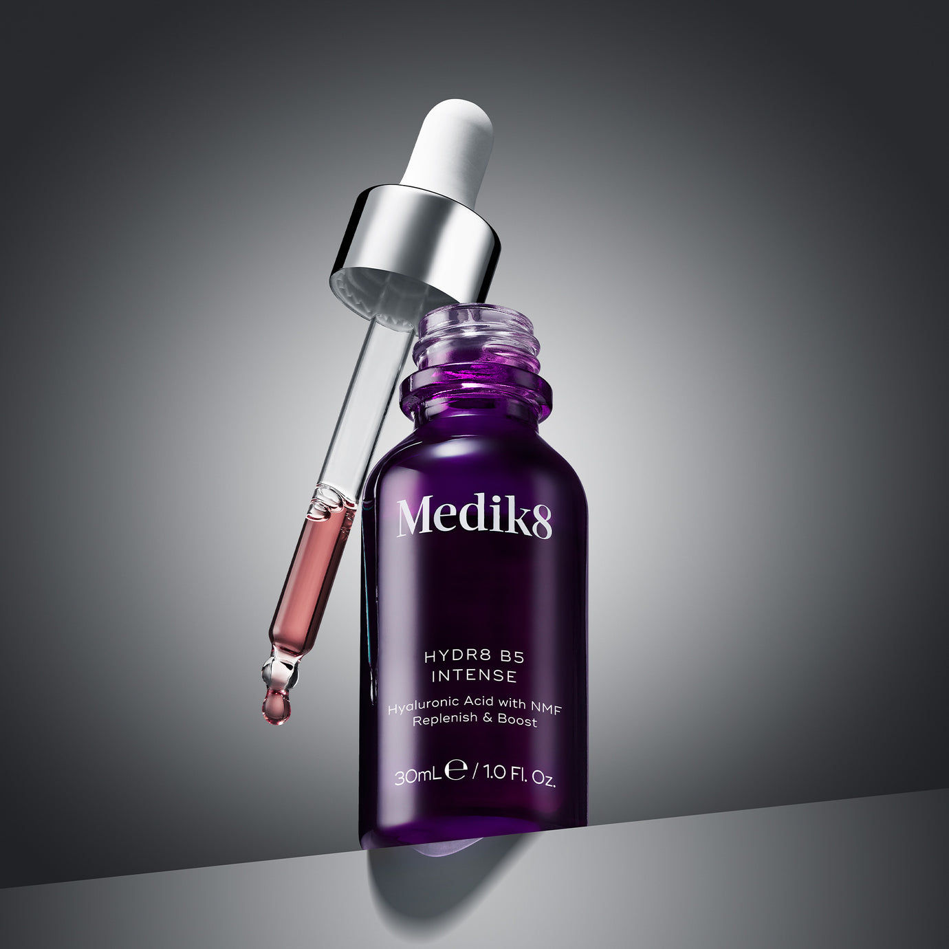 A professional photograph of an open purple glass bottle of Hydr8 B5 Intense with the dropper leaning against it, resting on a grey geometric surface against a grey gradient background. Below the image, clear text identifies this product category as ‘Serums’.