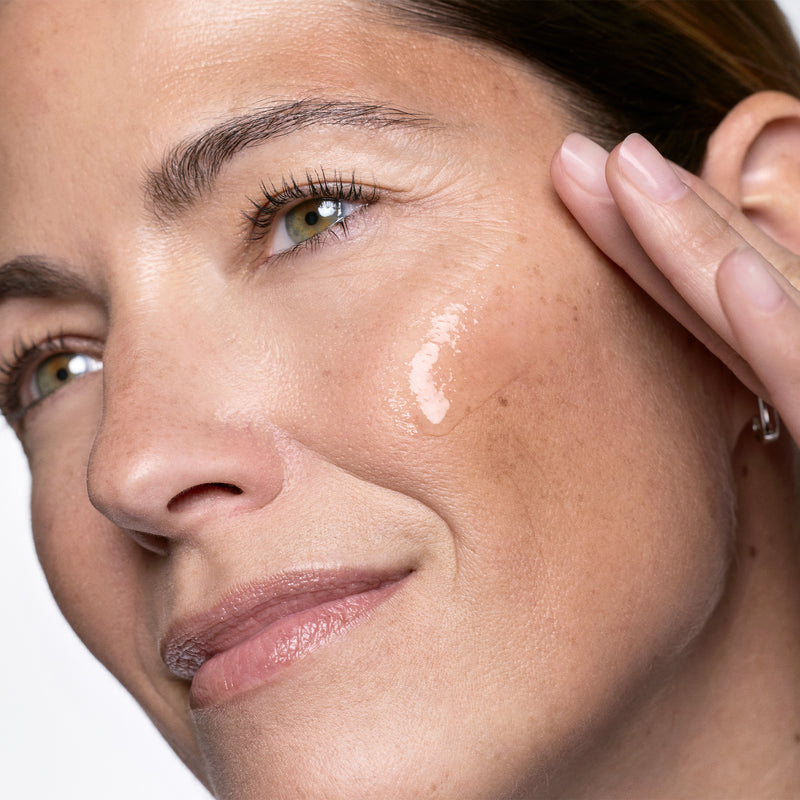 Close-up of a woman's face with a hand applying Exo-PDRN Prismatic+ t to her cheek.