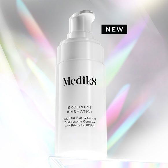 A white Medik8 Exo-PDRN Prismatic+ pump bottle resting on a clear prismatic surface against a light grey background with holographic, colourful light flares. A black badge reads "NEW". Text on the bottle details it as a "Youthful Vitality Serum Tri-Exosome Complex with Prismatic PDRN".-2