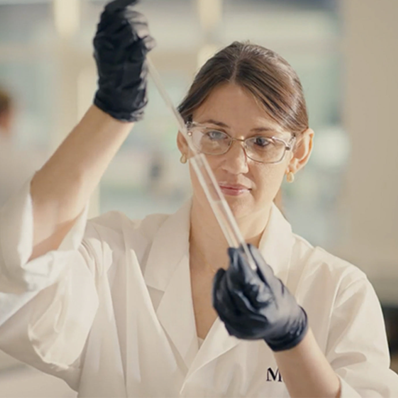 A close-up of a scientist in a white lab coat and protective eyewear, meticulously using a pipette in the Medik8 UK Innovation Centre.