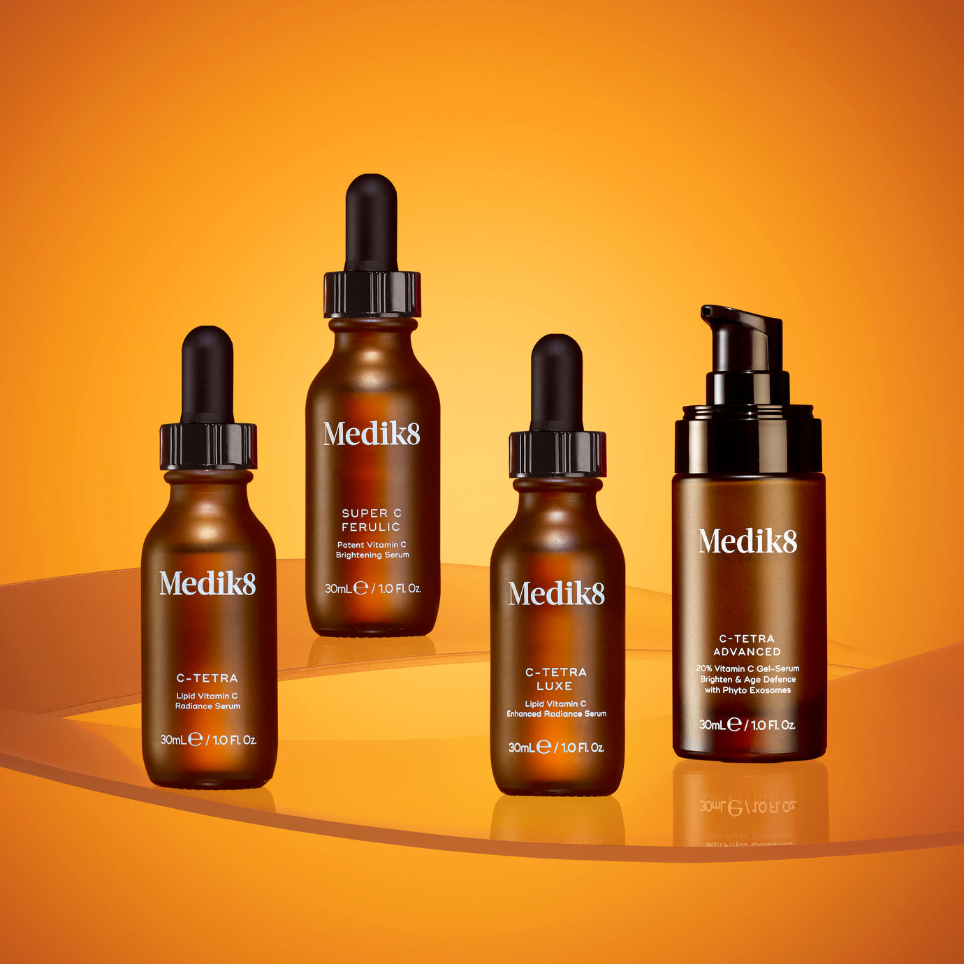 Four Medik8 vitamin C serums displayed on reflective, transparent orange tiers against a bright orange background. From left to right: C-Tetra amber dropper bottle, a Super C Ferulic amber dropper bottle, C-Tetra Luxe amber dropper bottle, and C-Tetra Advanced amber pump bottle.